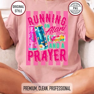 May include: Pale pink t-shirt featuring the slogan "RUNNING ON Alani AND A PRAYER" with images of Alani Nu energy drink cans. The design has a vertical striped background. The text and cans are in bright colours.