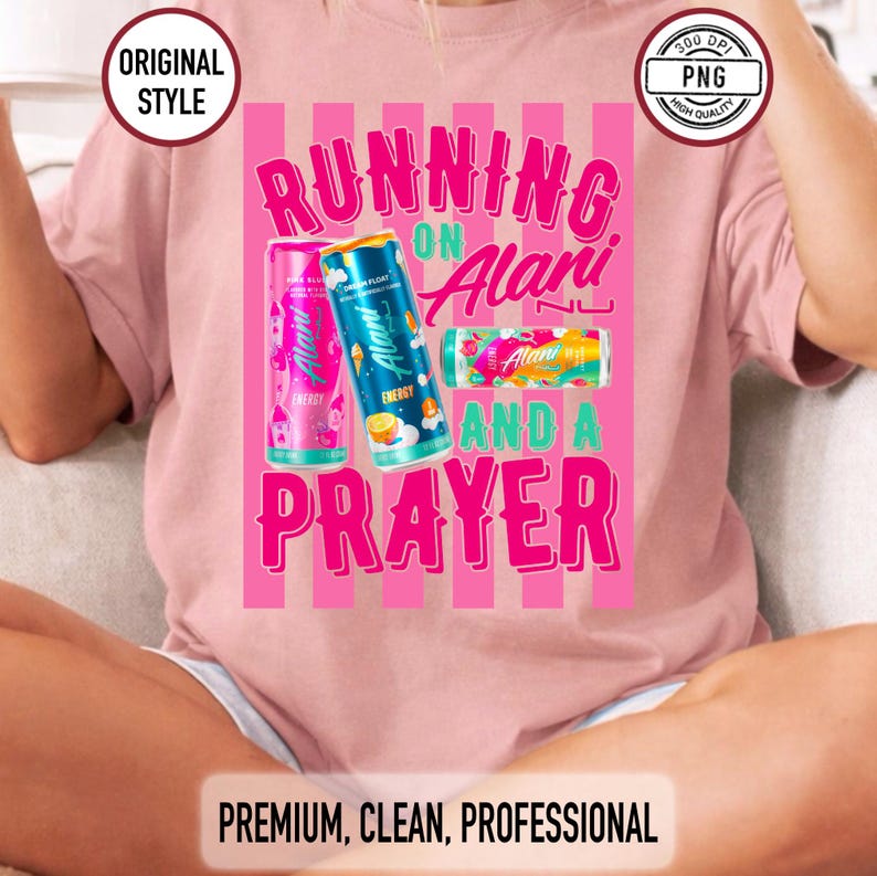 May include: Pale pink t-shirt featuring the slogan "RUNNING ON Alani AND A PRAYER" with images of Alani Nu energy drink cans. The design has a vertical striped background. The text and cans are in bright colours.