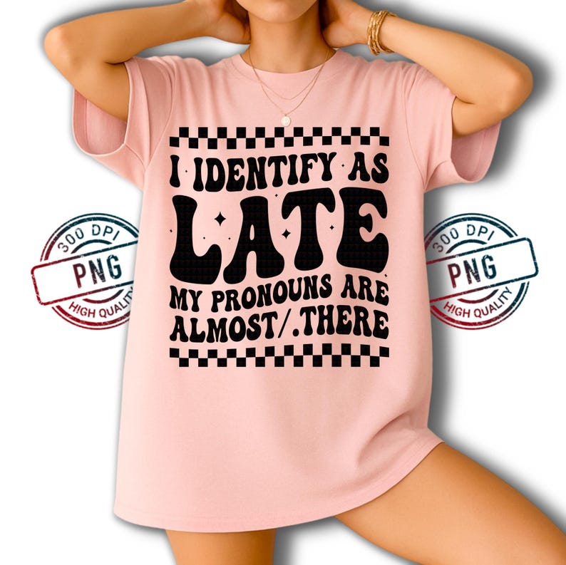May include: A light pink t-shirt with the text "I IDENTIFY AS LATE MY PRONOUNS ARE ALMOST/.THERE" in black, with a checkerboard pattern above and below the text. The shirt has short sleeves.