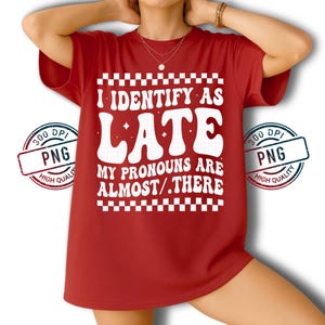 May include: A red t-shirt with the text "I IDENTIFY AS LATE, MY PRONOUNS ARE ALMOST/.THERE" in white, retro-style font. The design includes a checkered border and is printed on a high-quality PNG. The shirt is a casual wear item.