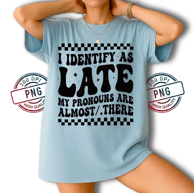 May include: Light blue t-shirt with the text "I IDENTIFY AS LATE MY PRONOUNS ARE ALMOST/.THERE" in black. The text is framed by a black and white checkered pattern. The shirt is a casual wear item.
