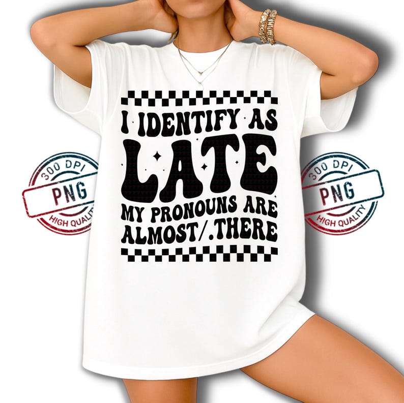 May include: White t-shirt with the text "I IDENTIFY AS LATE MY PRONOUNS ARE ALMOST/.THERE" in black, retro-style font. The design includes a checkered border and is printed on a white, short-sleeved shirt.