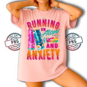 May include: A light pink t-shirt with the text "RUNNING ON Alani AND ANXIETY" in colorful letters. The shirt features three Alani Nu energy drink cans in pink, blue, and a multi-colored design.