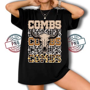 May include: Black t-shirt featuring the word "COMBS" in a stacked design with a bull skull graphic. The design incorporates leopard print and a neutral color palette. The shirt has a relaxed fit.