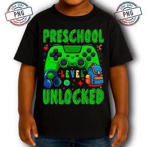 May include: Black t-shirt with a green graphic featuring a video game controller, headphones, and a backpack. The text reads "Preschool Level Unlocked" in green. The design includes an apple, scissors, and stars.