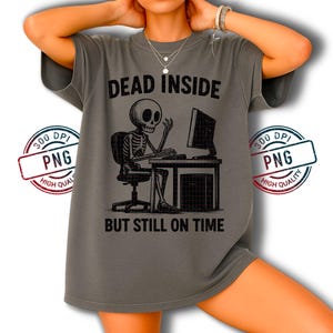 Puede incluir: Camiseta gris con el texto "DEAD INSIDE BUT STILL ON TIME" y un gráfico negro de un esqueleto sentado frente a una computadora. La camiseta tiene mangas cortas y un corte holgado.