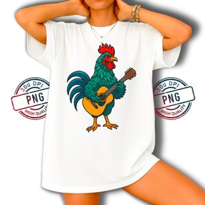 Op de afbeelding: Wit T-shirt met een cartoon haan die gitaar speelt. De haan heeft turquoise veren, een rode kam en gele poten. De gitaar is bruin en geel. Het T-shirt heeft een losse pasvorm.