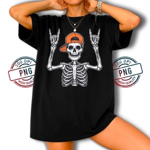 May include: Black t-shirt with a white skeleton graphic wearing an orange baseball cap and making a rock-and-roll hand gesture. The design includes a detailed rib cage and arms. The t-shirt has a relaxed fit.