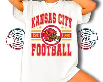 Könnte beinhalten: Weißes T-Shirt mit roter und goldener Grafik. Die Grafik zeigt "KANSAS CITY FOOTBALL" mit einem Football-Helm in der Mitte. Das Shirt hat auch den Text "EST. 1960".