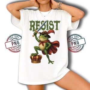May include: White t-shirt featuring the word "RESIST" in green, above a cartoon frog wearing a cape, hat, and holding a sword. The frog stands on a golden crown. The image has a "300 DPI PNG HIGH QUALITY" stamp.