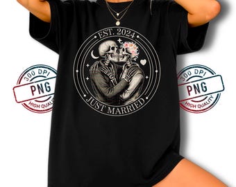 以下が含まれることがあります： 黒いTシャツ。円形のグラフィックには、花柄の装飾が施された2体の抱き合う骸骨が描かれています。「EST. 2024」と「JUST MARRIED」の文字が含まれています。Tシャツは半袖です。