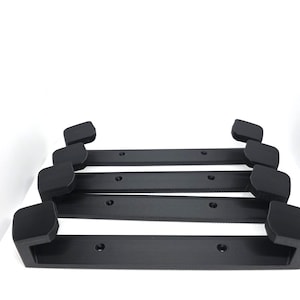 Puede incluir: Cuatro manijas negras y rectangulares con esquinas redondeadas y orificios pretaladrados. Las manijas están apiladas, con la manija superior ligeramente desplazada. El fondo es blanco liso.