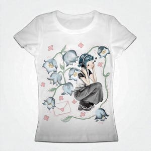 Peut inclure: T-shirt blanc avec une illustration à l'aquarelle d'une personne écoutant de la musique au casque, entourée de fleurs de jacinthes bleues et d'accents roses. Le motif comprend des notes de musique et une lettre avec un cœur.