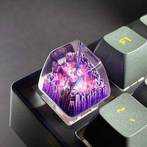 May include: A custom keyboard keycap featuring a miniature, detailed landscape design. The keycap is transparent, showcasing a purple mountain range with pink and purple accents, and a blue figure. The keycap is mounted on a black keyboard.