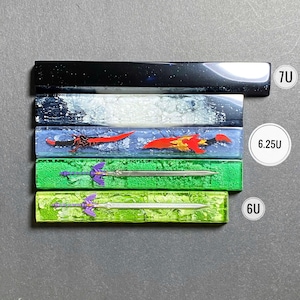 May include: A collection of custom keycaps with embedded designs. The keycaps feature various colors and designs, including a black and silver speckled, a blue and white speckled, and two with sword designs. The keycaps are labeled 7U, 6.25U, and 6U.