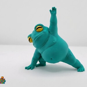 May include: A turquoise frog figurine in a yoga pose, with one arm raised and the other extended. The frog has large yellow eyes and a textured surface. The figurine is a whimsical decorative item.
