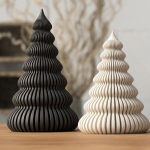 May include: Two decorative, stylized Christmas trees. One is black, the other is off-white. Both have a ridged, layered design and a pointed top. They are displayed on a wooden surface, suggesting a holiday or seasonal theme.