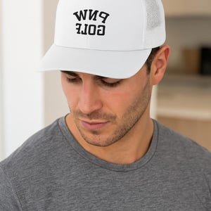 May include: White trucker cap with a curved peak and mesh back. The cap has the text "CORE BIM" in black block letters. The person in the image is wearing a grey t-shirt.