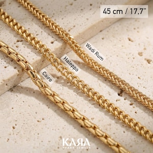 May include: Close-up of three gold-colored chain necklaces. The necklaces are labeled "Cairo", "Aleppo", and "Wadi Rum". The top necklace is 17.7 inches (45 cm) long. The brand name "KARA Spark Jewels" is at the bottom.