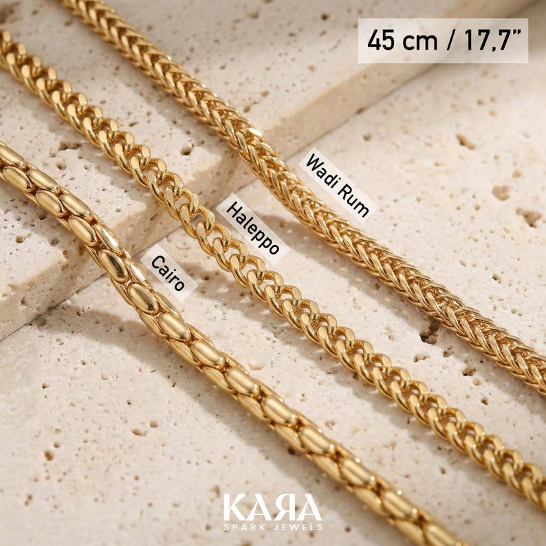 May include: Close-up of three gold-colored chain necklaces. The necklaces are labeled "Cairo", "Aleppo", and "Wadi Rum". The top necklace is 17.7 inches (45 cm) long. The brand name "KARA Spark Jewels" is at the bottom.
