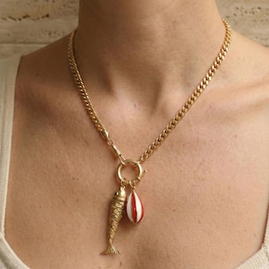May include: Gold-toned necklace with a chunky chain. The pendant features a detailed fish charm and a red and white striped teardrop charm. The necklace is secured with a large clasp.