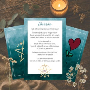 Könnte beinhalten: Drei teal- und weißfarbene Karten mit goldenen Akzenten und Text, angeordnet auf einer Holzoberfläche mit einer brennenden Kerze und Blättern. Die Karten zeigen das Wort "Charisma" und inspirierenden Text. Eine Karte hat eine rote Herzillustration.