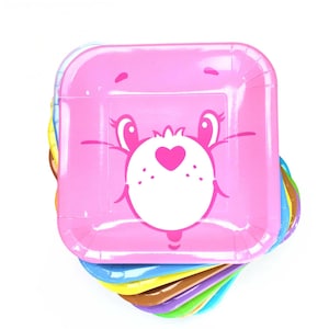 May include: A stack of colorful square paper plates. The top plate is pink and features a cartoon bear face with a heart on its chest. The plates below are various colors, including blue, yellow, and brown.