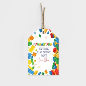 May include: A white gift tag with a colorful Lego-themed design. The tag features the text "THANK YOU FOR COMING TO MY BIRTHDAY PARTY! Love, Oliver." The tag is decorated with various colored Lego bricks and confetti.