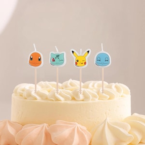 May include: A yellow frosted cake with four character-themed candles. The candles feature cartoon characters in orange, green, yellow, and blue. The cake is decorated with white frosting swirls and sits on a white surface.