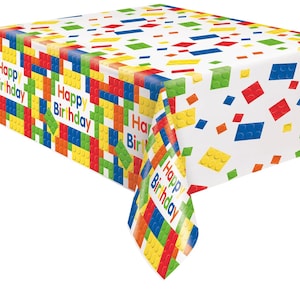 May include: A white rectangular tablecloth with a colorful pattern of toy building blocks in red, blue, yellow, green, and orange. The words "Happy Birthday" are printed on the tablecloth.
