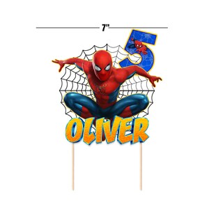 Może przedstawiać: Topper na ciasto z motywem Spidermana. Projekt przedstawia Spidermana w dynamicznej pozie, cyfrę 5 oraz imię "Oliver" w pomarańczowych i ż&oacute;łtych literach. Topper ma szerokość około 17.78 cm.