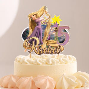May include: A birthday cake with a Rapunzel-themed topper. The topper features a cartoon of Rapunzel with long blonde hair, a purple dress, and the name "Rachel" and the number "5". The cake is decorated with white frosting and pink meringues.