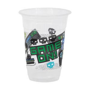 May include: A clear plastic cup with a white rim and a gaming-themed design. The design includes the words "GAME ON!" in green block letters, along with pixelated skulls, a controller, and other gaming graphics.