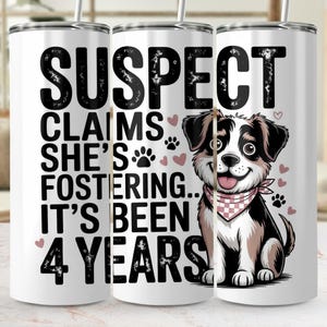 Peut inclure: Gobelet en acier inoxydable blanc avec le texte "SUSPECT CLAIMS SHE'S FOSTERING... IT'S BEEN 4 YEARS" et une illustration de chien de dessin animé. Le chien porte un bandana rose et blanc et des empreintes de pattes.