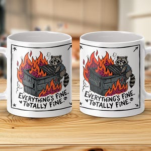 Puede incluir: Taza de cerámica blanca con un mapache de dibujos animados en un contenedor de basura en llamas. El diseño incluye llamas naranjas y el texto "Everything's Fine. Totally Fine." La taza tiene un asa blanca.