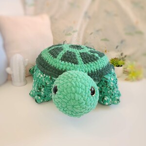 Op de afbeelding: Een groen gehaakt schildpad speelgoed met zwarte ogen. De schildpad heeft een getextureerde schil en een zacht, pluche lichaam.