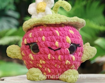Puede incluir: Un peluche de fresa hecho a mano con ganchillo. El juguete tiene un cuerpo rosa con detalles de semillas amarillas, hojas verdes y una flor blanca y amarilla. Tiene ojos grandes y brazos y pies pequeños. El juguete está diseñado para parecerse a una fresa de dibujos animados.
