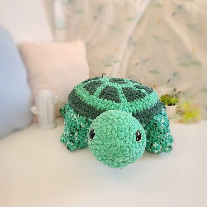 Op de afbeelding: Een groen gehaakt schildpad speelgoed met zwarte ogen. De schildpad heeft een getextureerde schil en een zacht, pluche lichaam.