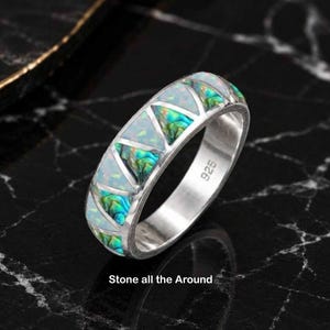 Peut inclure: Une bague en argent avec un poinçon 925, présentant un motif alterné d'incrustations triangulaires en opale blanche et en nacre d'ormeau verte irisée. L'anneau est conçu avec ces incrustations de pierre tout autour de la circonférence.