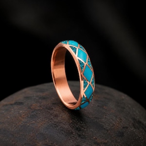 May include: A copper ring featuring a diamond-shaped lattice pattern inlaid with bright turquoise stone fragments. The band has a smooth, polished metallic finish on the interior and edges, contrasting with the textured blue stone inlay.