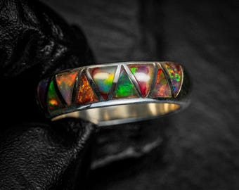 May include: Silver ring with a band featuring triangular inlays of vibrant, multicolored opal. The opal displays a spectrum of colors, including orange, green, and red, set against a dark background. The ring's design is modern and eye-catching.