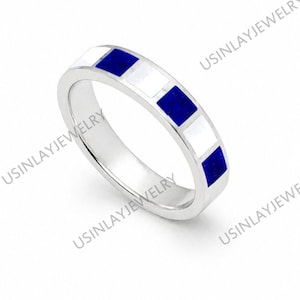 Può includere: Un anello d'argento con un motivo ripetuto di quadrati bianchi e blu. L'anello è a fascia, con i quadrati uniformemente distanziati attorno alla circonferenza. L'anello è su uno sfondo bianco.