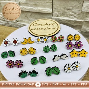 Può includere: Una collezione di orecchini a lobo in legno con vari disegni, tra cui fiori, soli, lune, foglie, nuvole e stelle. Gli orecchini sono dipinti con colori vivaci. L'immagine include anche il testo "Cre Art LaserWood".