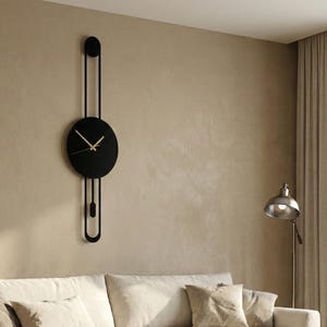 May include: A modern living room featuring a black wall clock with a circular face and gold hands. A beige sofa with throw pillows and a blanket sits below the clock. A wooden coffee table and a round jute rug complete the scene.