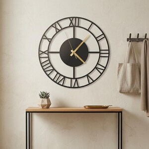 May include: A large, black metal wall clock with Roman numerals hangs above a wooden console table. The clock has gold-colored hands and a black center. A small succulent in a geometric pot sits on the table.