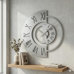 Könnte beinhalten: Eine große, silberfarbene Wanduhr mit römischen Ziffern. Die Uhr hat ein einzigartiges, halbkreisförmiges Design mit einem kleineren, inneren Zifferblatt. Die Zeiger sind silberfarben, und die Uhr ist an einer hellgrauen Wand befestigt. Ein Holzregal darunter enthält Bücher und eine Vase.