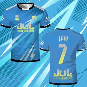 May include: A short-sleeved blue t-shirt featuring a graphic print with the text JUL RIEN 100 RIEN on the front and TOTO 7 JUL on the back. The design includes an alien icon, geometric patterns, and black trim on the crew neck and sleeve cuffs.