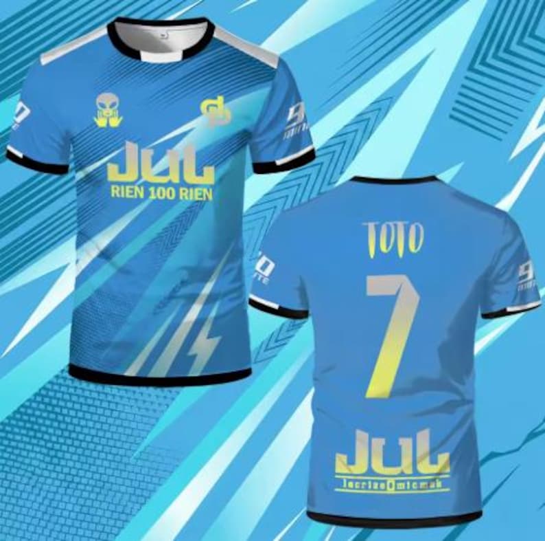May include: A short-sleeved blue t-shirt featuring a graphic print with the text JUL RIEN 100 RIEN on the front and TOTO 7 JUL on the back. The design includes an alien icon, geometric patterns, and black trim on the crew neck and sleeve cuffs.