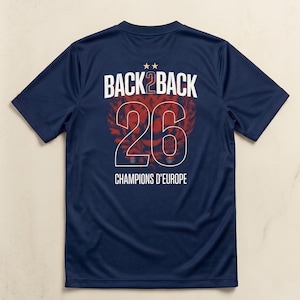 May include: A navy blue short-sleeved t-shirt featuring a graphic on the back. The design includes the white text BACK 2 BACK, two small stars, the large number 26 in white outline, and the text CHAMPIONS D'EUROPE in white below the number.
