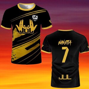 May include: A black and gold short-sleeve t-shirt featuring a graphic of hand gestures and the text JUL on the front. The back displays the name NINETTA above the number 7 and the text JUL in gold lettering, with gold trim on the collar and sleeves.
